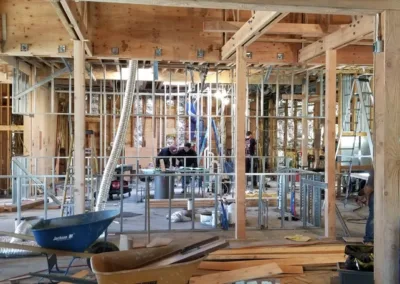 Workers are actively constructing the interior framework of a building, with wood beams, metal studs, and various construction tools scattered throughout the site.