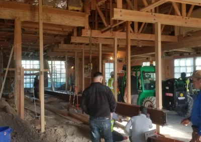 Several construction workers are inside a building under renovation with exposed wooden beams and a green forklift in the background.